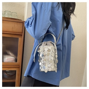 Detail of silver sequin bucket bag with drawstring liner and chain strap worn by model