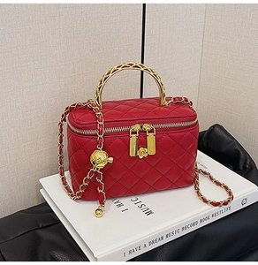 Detail of red quilted crossbody bag with gold chain strap and floral metal charm
