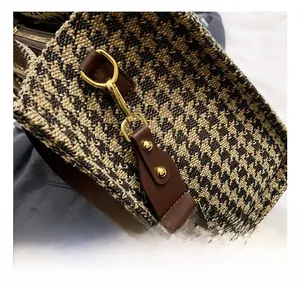 Detail shot of golden metal hook on houndstooth crossbody bag with brown leather trim