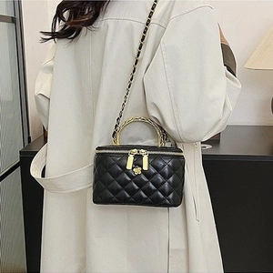Quilted black leather mini vanity bag with gold chain strap and top handle on a beige trench coat