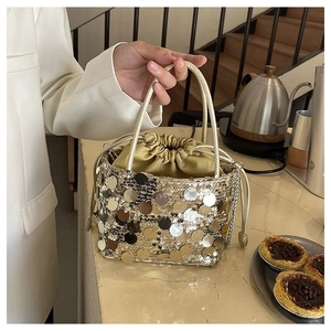 Detailed close-up of a gold bucket bag featuring sparkling sequins and a drawstring lining
