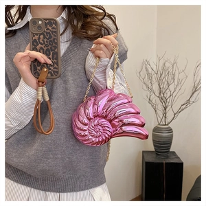 Détail du sac pochette coquillage rose métallisé avec chaîne dorée par le mannequin