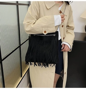Detail of black suede fringe crossbody bag with silver chain strap on beige coat
