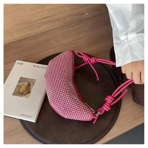 Detalle del bolso hobo fucsia con brillantes pedrería y correa anudada sobre una revista