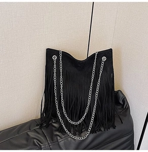 Close-up of black fringe shoulder bag with silver chain straps on textured surface