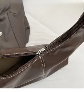Detailed close-up of smooth silver metal zipper on premium brown leather shoulder bag