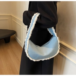 Détail du sac croissant en denim bleu clair avec franges blanches porté sur un manteau