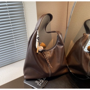 Detailed view of brown leather hobo bag with baseball charm and contrast stitching