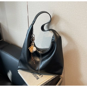 Chic black crescent shoulder bag with contrast stitching and baseball charm on a book
