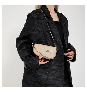 Dettaglio borsa a tracolla beige con fiocco argento e catena su un blazer nero di classe