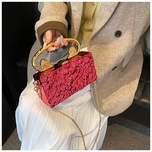 Detail of red wrinkled evening bag featuring a gold lion head handle and fine metal chain