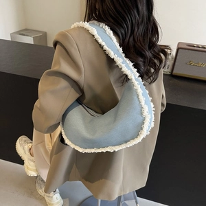 Sac croissant en denim bleu clair avec franges blanches porté à l'épaule pour un style chic