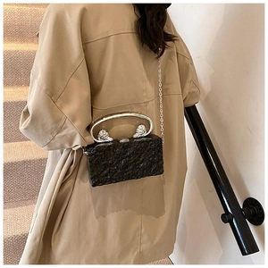 Detail of black rock pattern acrylic box bag with silver lion head handle on trench coat