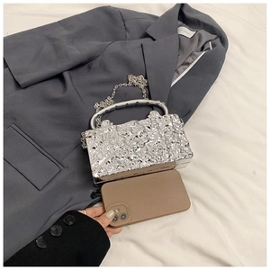 Detail of silver lava texture clutch bag with metal handle and chain strap for scale