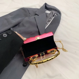 Magenta acrylic clutch with gold handle and chain on stylish grey blazer background