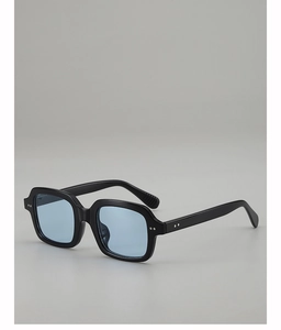 Close-up of black thick square frame sunglasses with light blue lenses and metal rivets