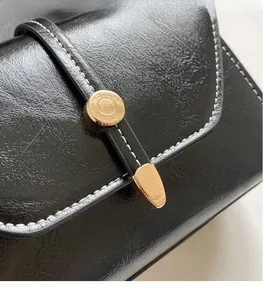 Detail of black oil wax leather handbag featuring contrast stitching and gold metal buckle