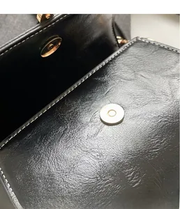 Close-up of black oil wax leather bag with round magnetic metal clasp and neat stitching