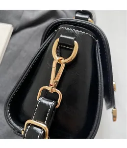 Detailed close-up of golden metal hooks and white contrast stitching on black leather bag