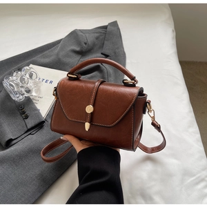 Detail view of brown leather bag featuring white contrast stitching and gold buckle