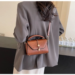 Rear view of a stylish brown leather crossbody bag with top handle and gold clasp hardware