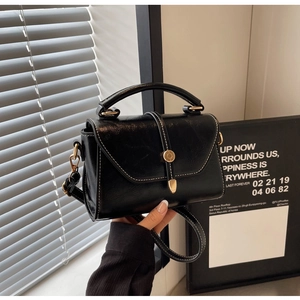 Detail of black crossbody bag with white contrast stitching and gold ring closure