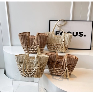 Détail de cabas en paille tissée de diverses couleurs avec pompons bohèmes et perles en bois