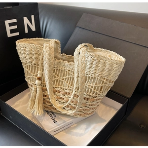 Détail d'un sac à main tressé beige avec motifs en losanges et pompons en perles de bois