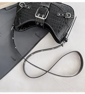 Détail de bandoulière réglable et boucle argentée sur sac noir à motif crocodile