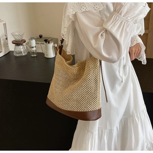 Detail view of a straw bucket bag with dark brown leather base on a shoulder strap