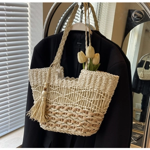 Détail d'un sac cabas en paille tressée beige et brun avec pompon et bandoulière texturée
