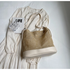 Detail of woven straw shoulder bag with creamy white leather straps on white dress