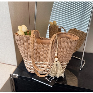 Grand sac cabas tressé avec pompon beige et doubles anses sur table en bois