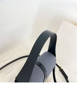 Detail of grey fabric handbag with black leather handle and adjustable shoulder strap