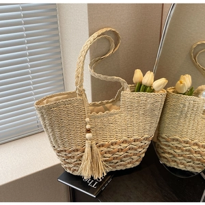 Détail d'un sac à main bohème en paille avec texture tissée, pompons et perles en bois