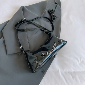 Detail of black patent leather crossbody bag with silver chains and rivets on grey blazer