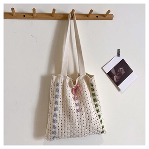Detail of hand-knitted cream tote bag with colorful stitching and pink drawstring bow