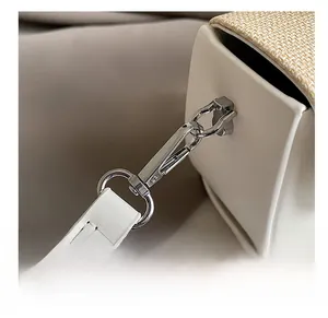 Macro shot of silver metal swivel hook and stitching on white leather handbag strap
