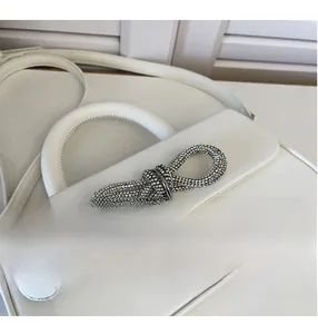Detailed close-up of a white leather handbag with a luxury crystal-set bow buckle decoration