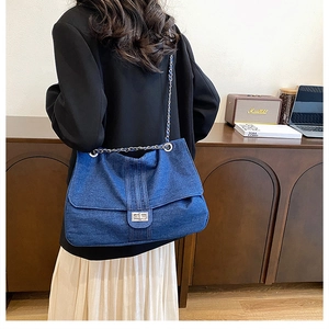 Detail of the large denim shoulder bag with silver turn-lock and chain strap on model