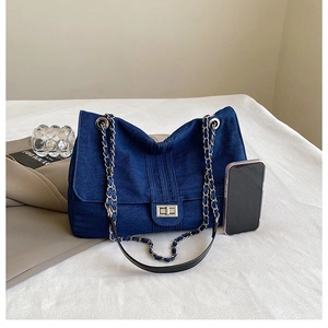 Detailed shot of dark blue denim shoulder bag with silver metal twist lock and chain strap