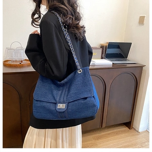 Detail of blue denim tote bag featuring silver square twist lock and metal chain strap