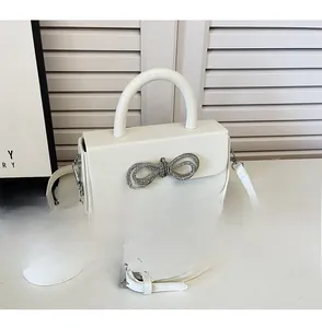 Detail of cream white crossbody box bag with rhinestone bow and phone for size reference