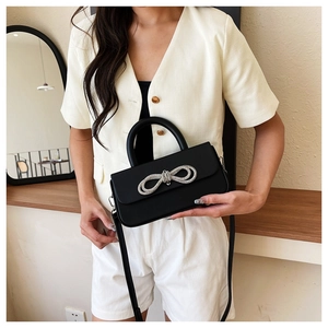 Detail of a black leather handbag featuring a sparkling double silver rhinestone bow accent