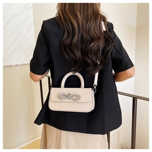 Detail view of cream crossbody bag with sparkling rhinestone bow on model back