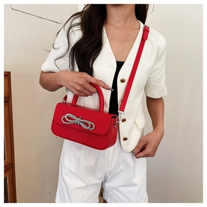 Detail of red crossbody bag with silver rhinestone bow on white outfit model