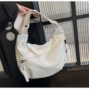 Détail du sac croissant en nylon blanc montrant le zip noir et la sangle tissée