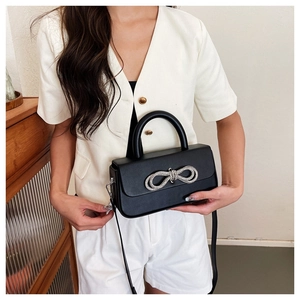Detail of black leather shoulder bag with a silver rhinestone bow and sleek silver hardware