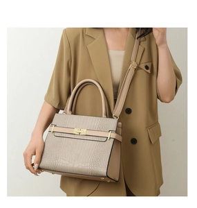 Detail of beige faux crocodile leather handbag with golden twist lock on khaki blazer