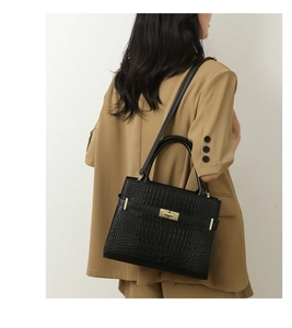 Detailed view of black crocodile pattern handbag with gold hardware on a model